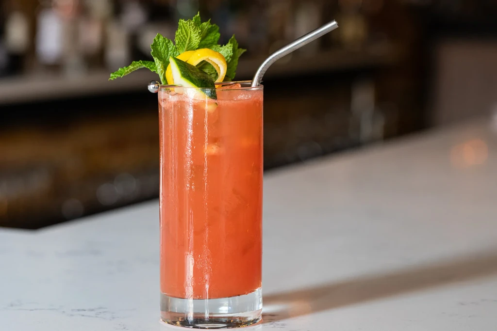 Cocktail with mint, lemon, and fruit slice on a white counter.