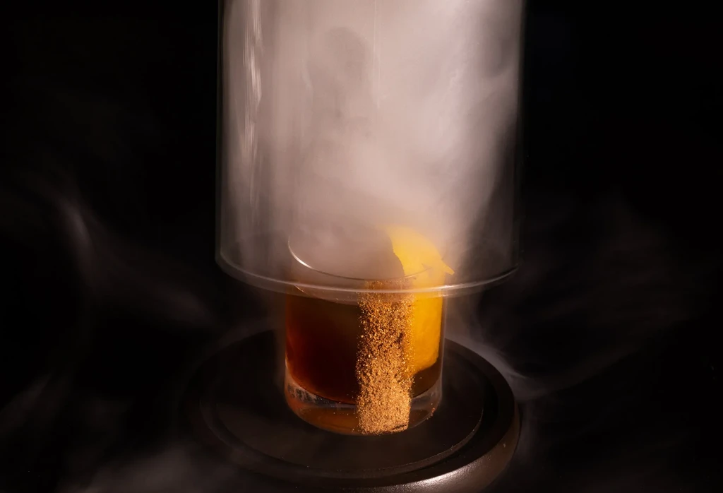 Smoked cocktail in a cloche with an orange peel garnish.