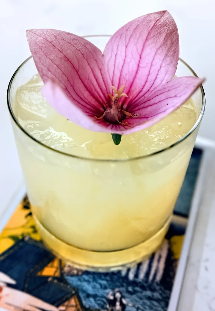 Yellow drink with ice, garnished with a pink flower.