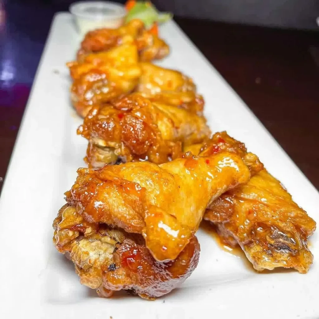 Glazed chicken wings on a white plate with dipping sauce.