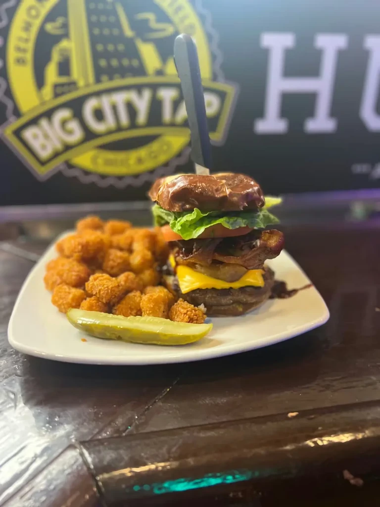Plate with a tall burger, tater tots, and a pickle spear.