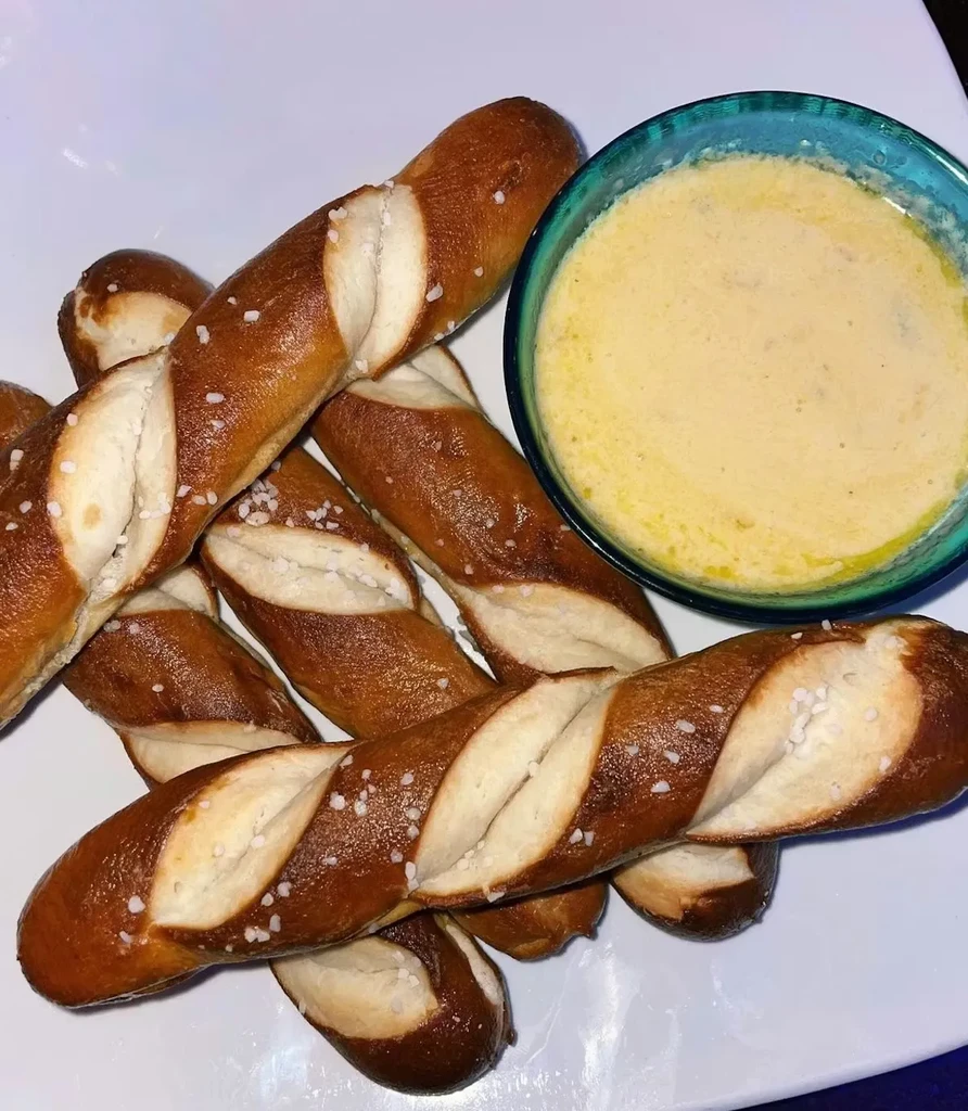 Pretzel sticks with coarse salt and dipping sauce on a white plate.