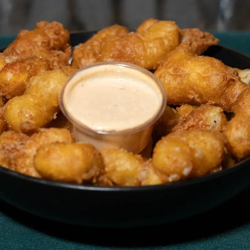 Deep-fried food in a black bowl with dipping sauce.