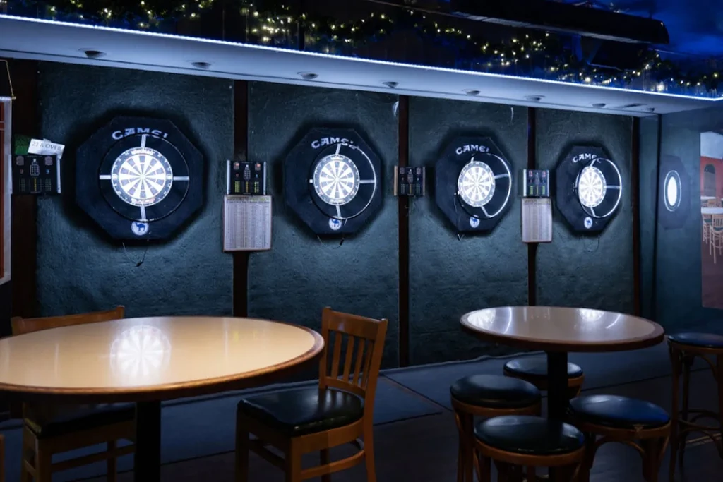 Four illuminated dartboards with digital scoreboards and camel logos in a bar.