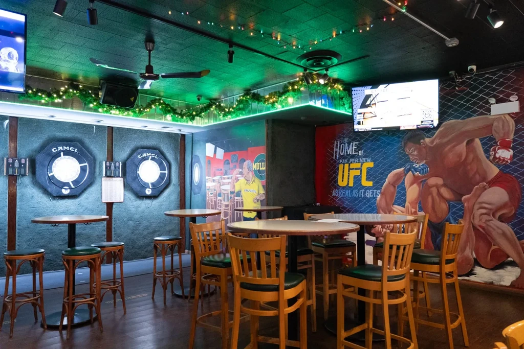 Interior of a sports bar with dartboards and MMA mural.