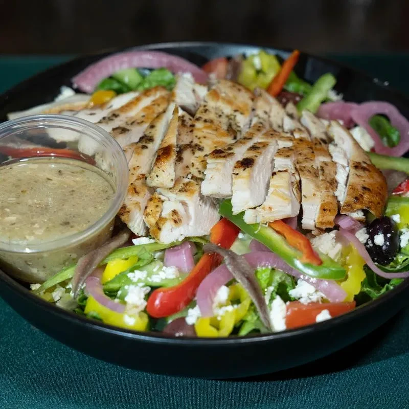 Grilled chicken salad with peppers, olives, cheese, and dressing.