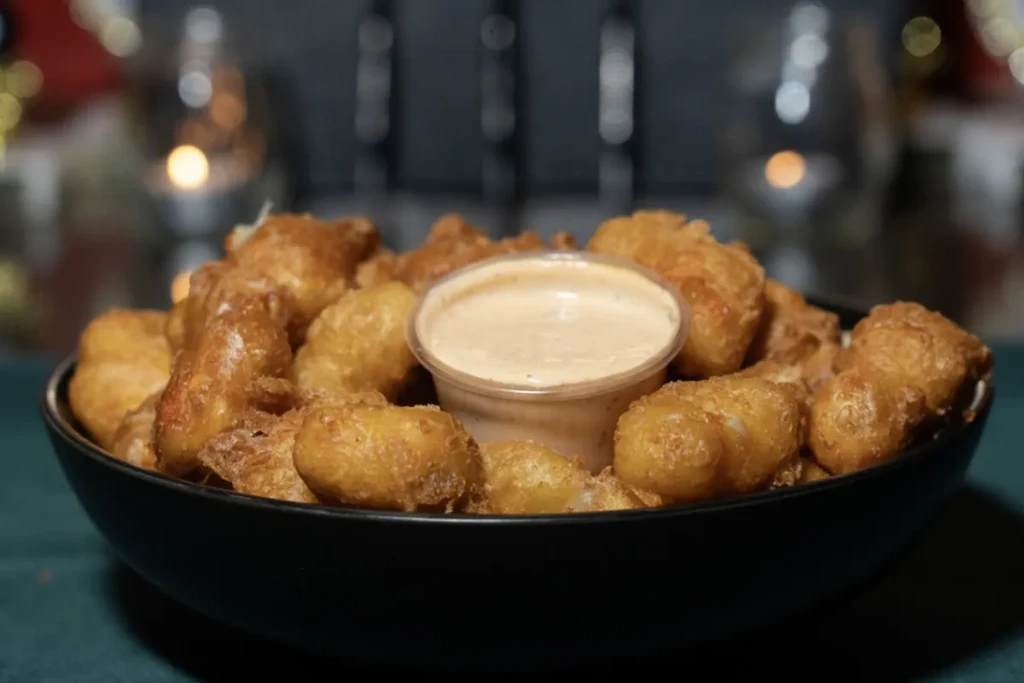 Deep-fried appetizers in a black bowl with a cup of dipping sauce.