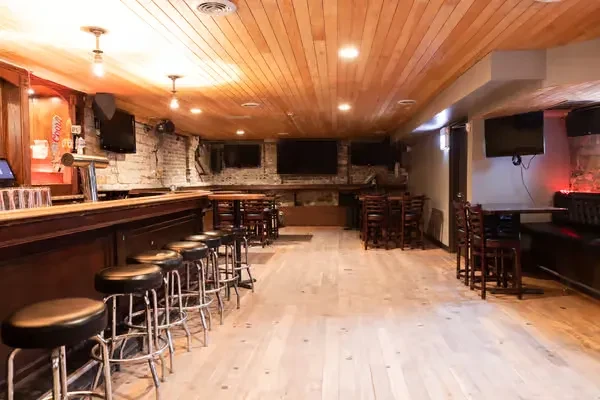 Rustic bar interior with wooden furnishings, brick walls, and TVs.