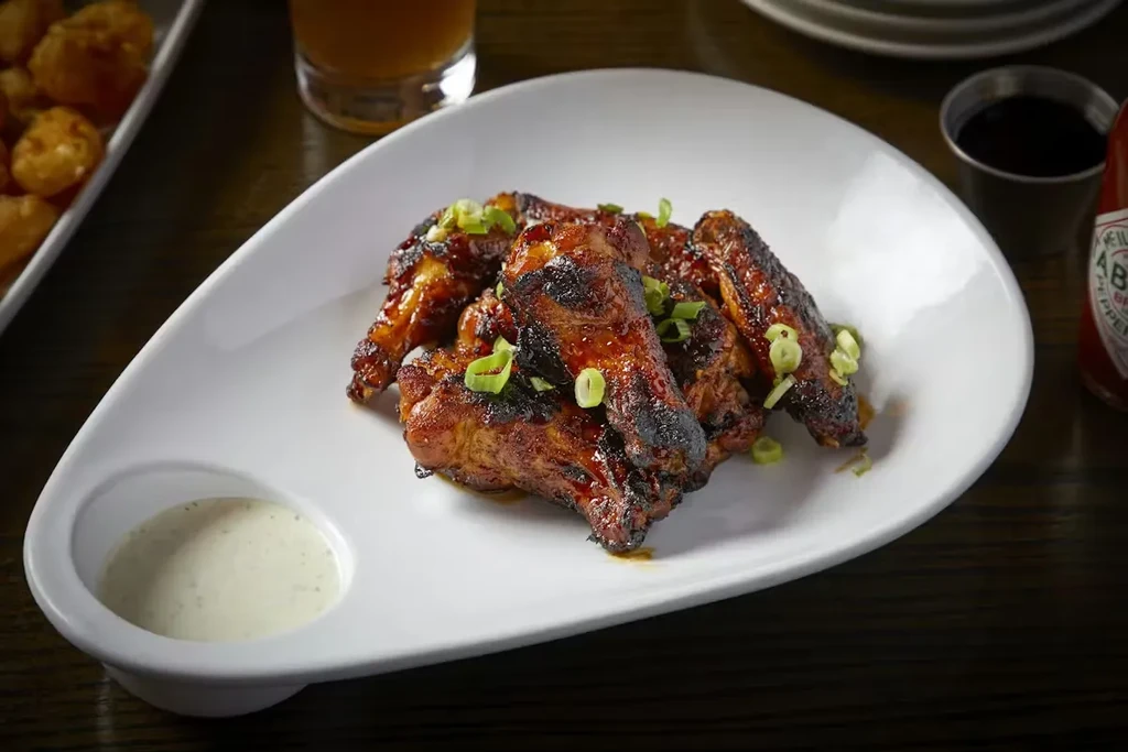 Barbecued chicken wings with dipping sauce on a pear-shaped plate.