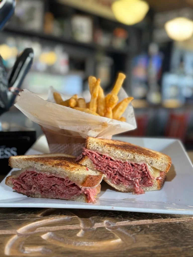 Grilled sandwich cut in half, with fries, on a white plate.
