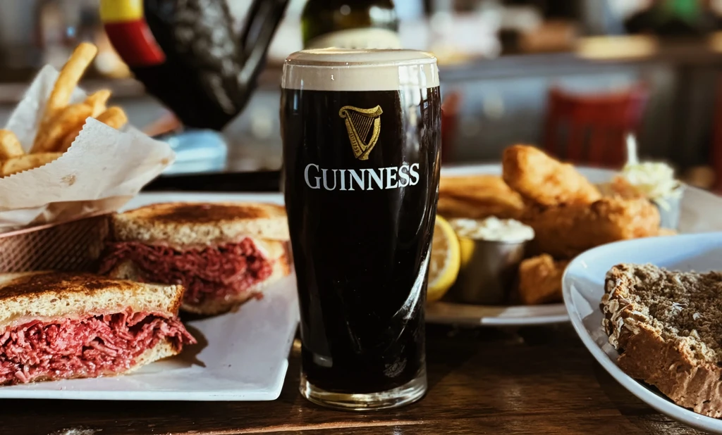 Guinness beer, corned beef sandwich, fries, and fried fish on a table.
