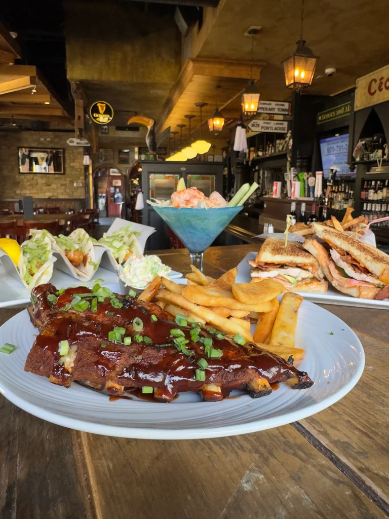 Barbecue ribs, tacos, shrimp cocktail, and sandwiches on a wooden table.