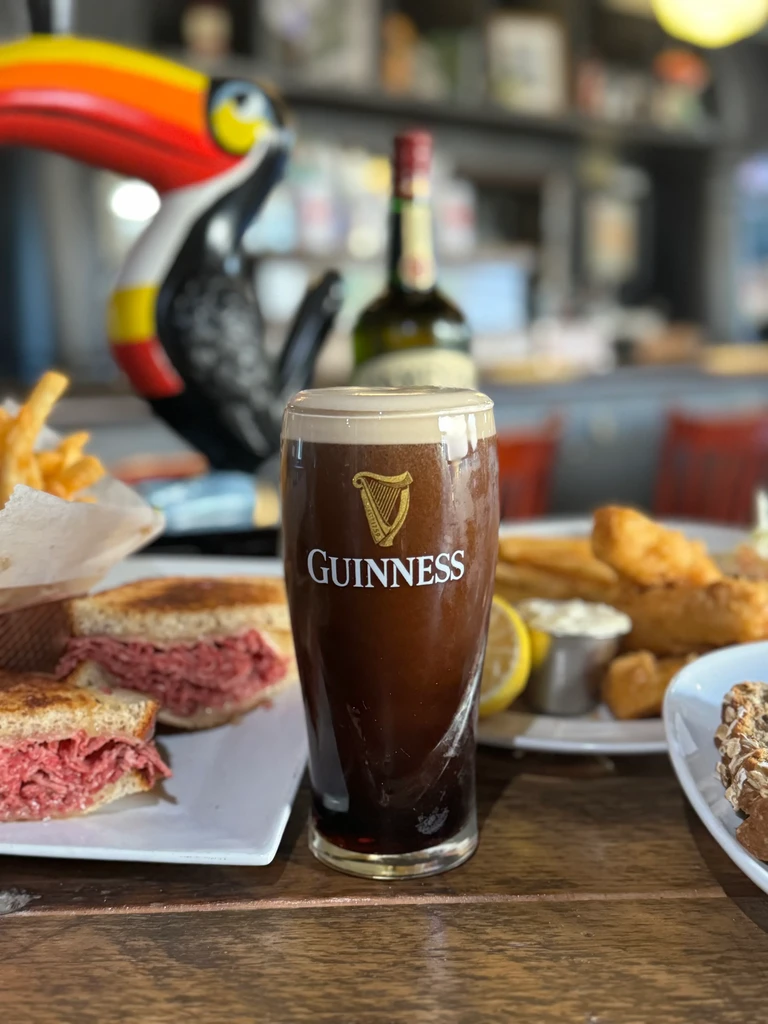 Guinness pint, grilled sandwich, and fries on a wooden table.