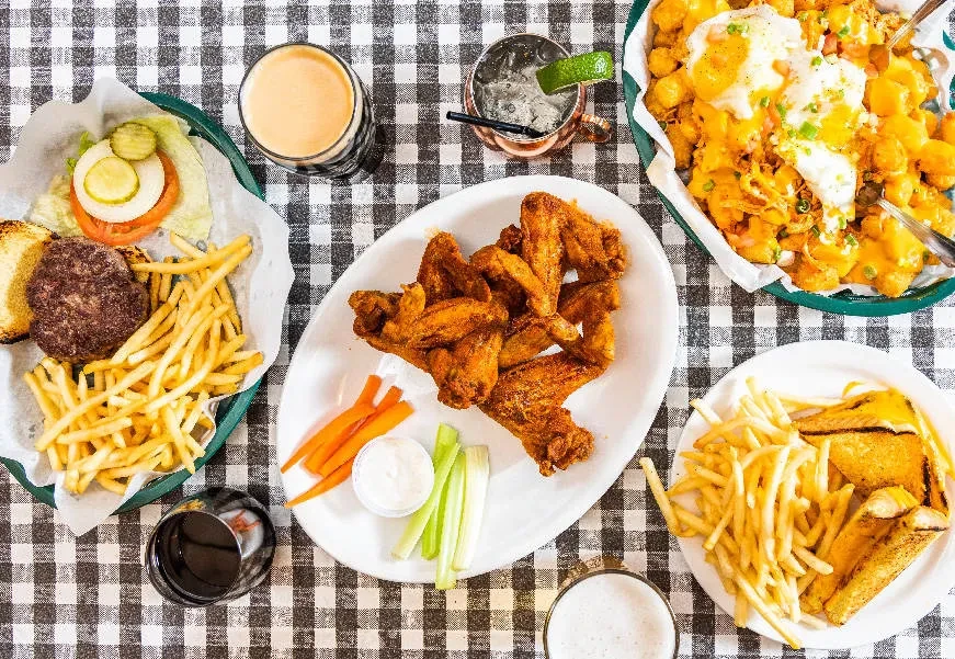 Table laden with burger, fries, wings, tots, beer, and drinks.