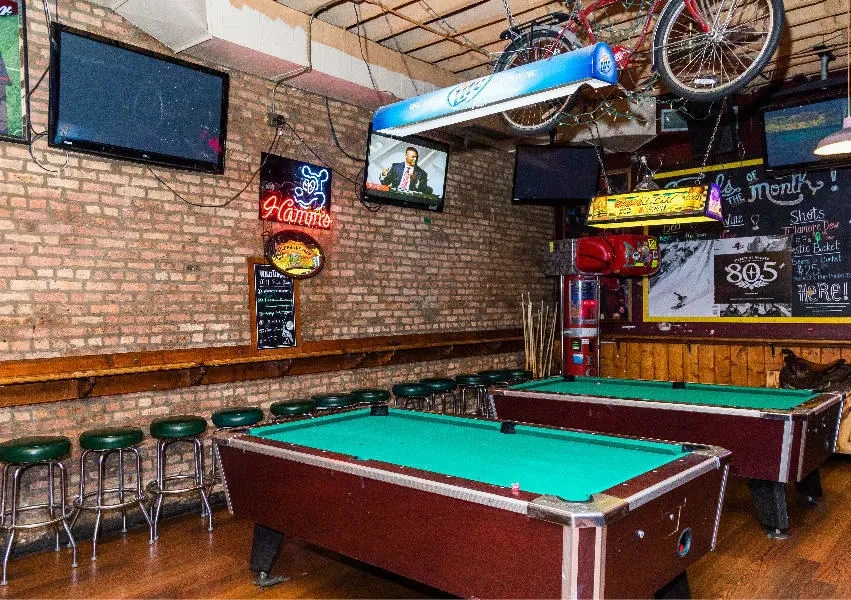 Interior of a casual bar with two pool tables and exposed brick.