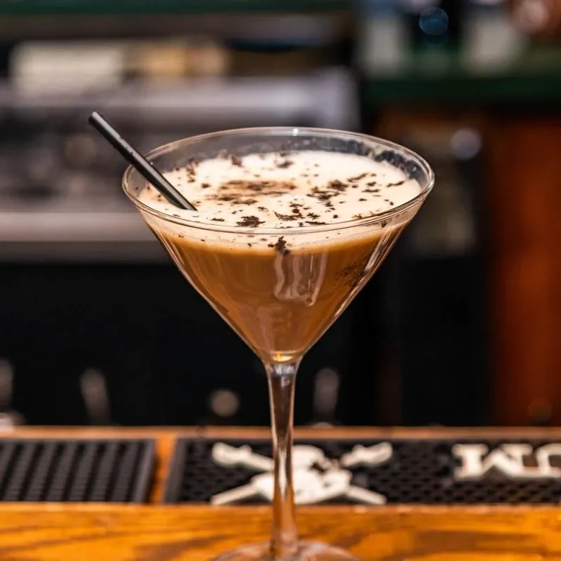 Martini glass with a creamy, brown drink, foam, and dark flakes.