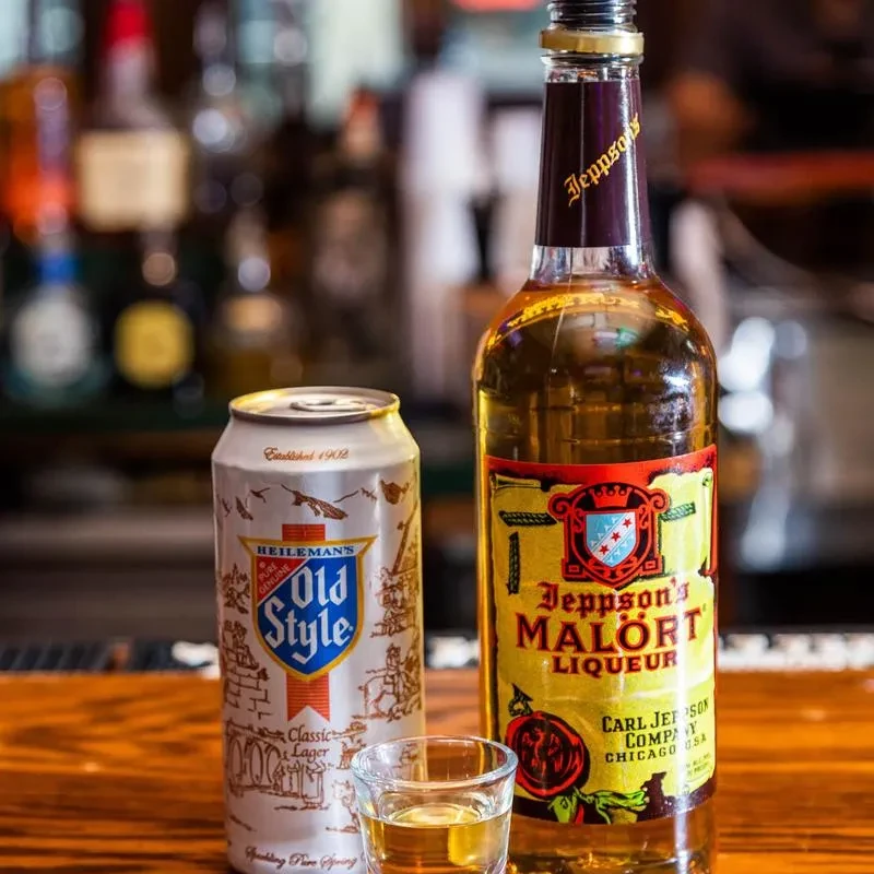 Old Style beer can, Malört bottle, shot glass on a wooden bar.