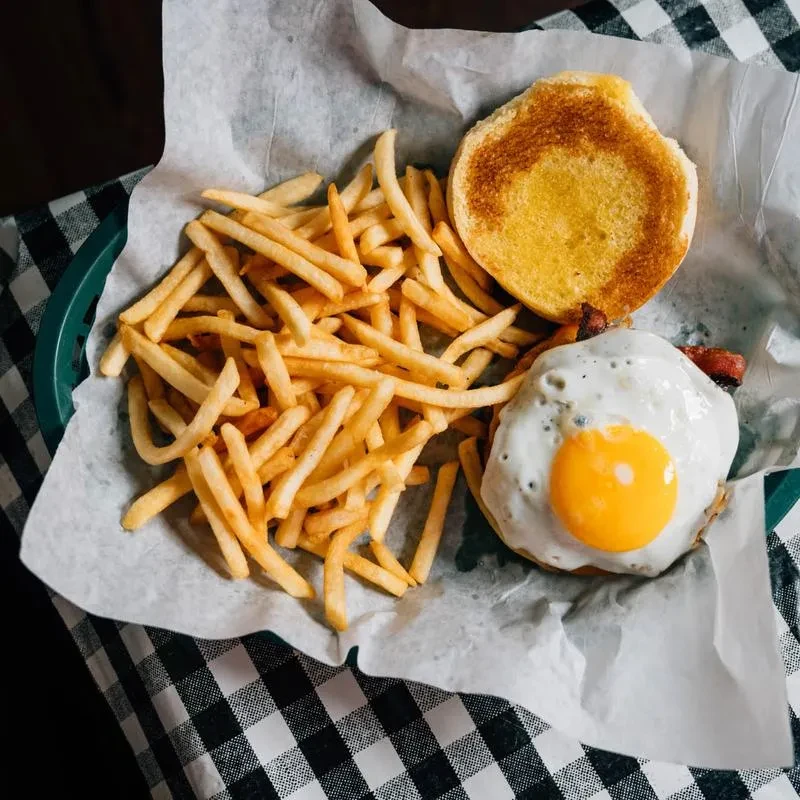 Burger with a fried egg, bacon, fries, and a toasted bun.
