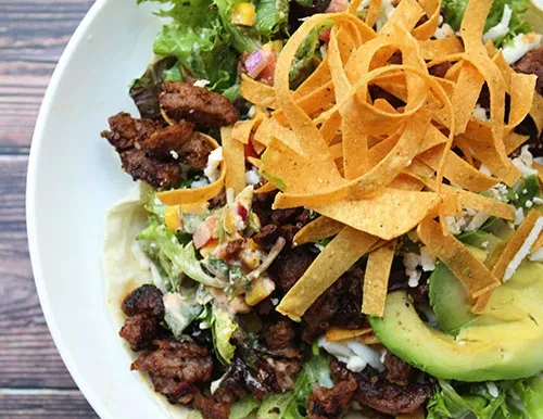 Close-up of a taco salad in a white bowl on a wooden surface.