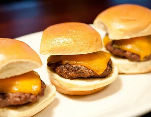 Three mini cheeseburger sliders with melted cheese on a white plate.