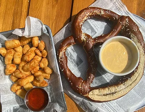 Tater tots and a soft pretzel with dipping sauces on a wooden table.