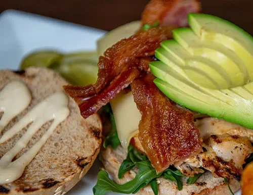 Open-faced chicken sandwich with arugula, bacon, cheese, and avocado.
