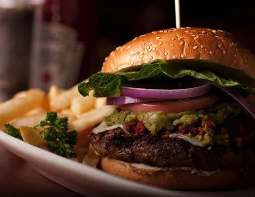 Gourmet burger with guacamole, sun-dried tomatoes, fries, and parsley.