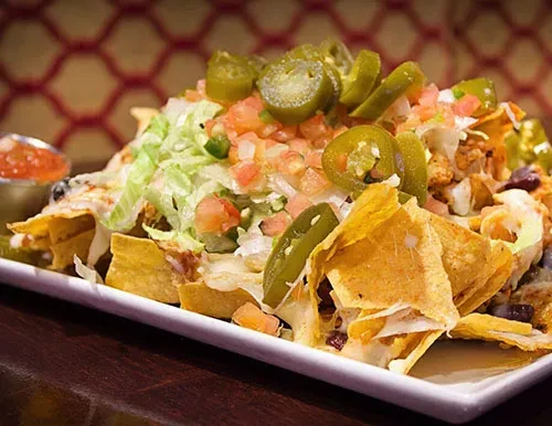 Close-up of nachos with cheese, lettuce, tomatoes, jalapeños, and salsa.