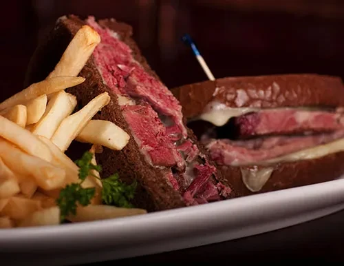 Roast beef sandwich with french fries and parsley on a white plate.