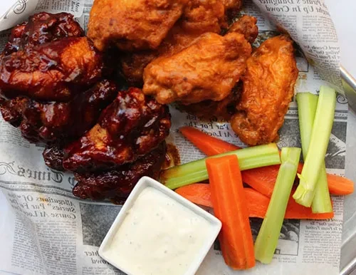 Two piles of chicken wings: BBQ and fried, with dip and vegetables.