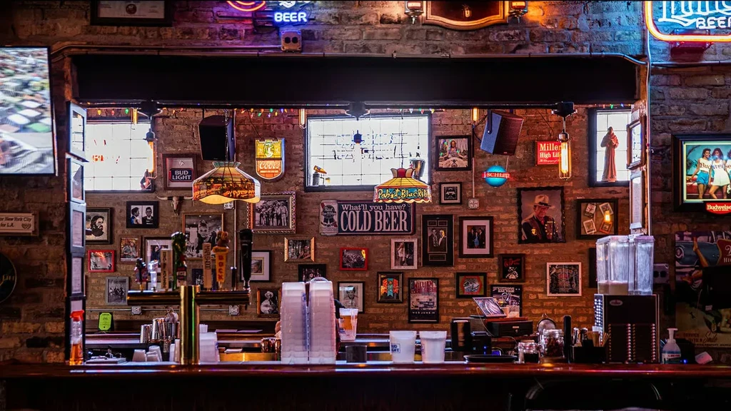 Rustic bar interior with brick wall, framed art, neon signs.