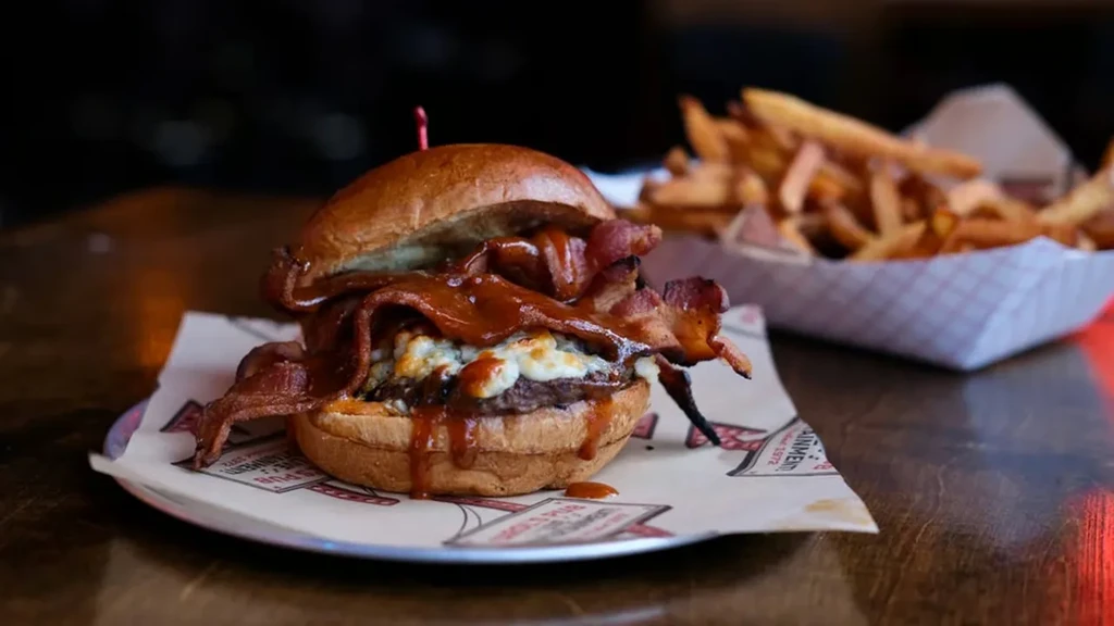 Gourmet burger with melted cheese, bacon, and sauce on a tray.
