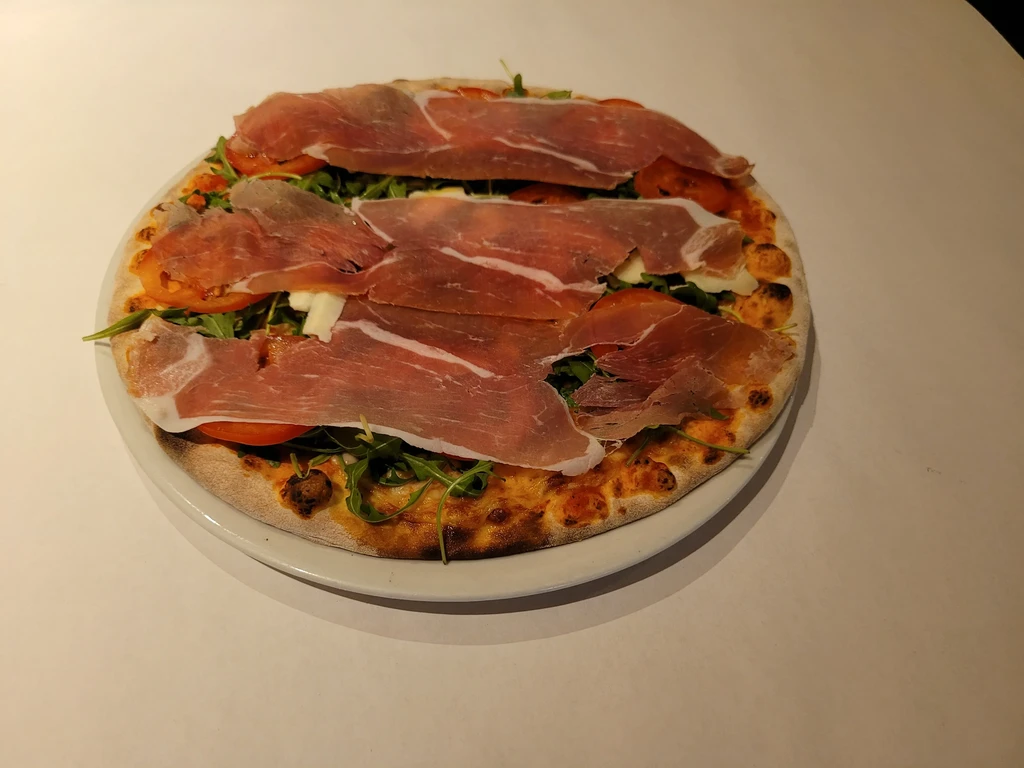 Wood-fired pizza with arugula, tomatoes, mozzarella, and prosciutto.