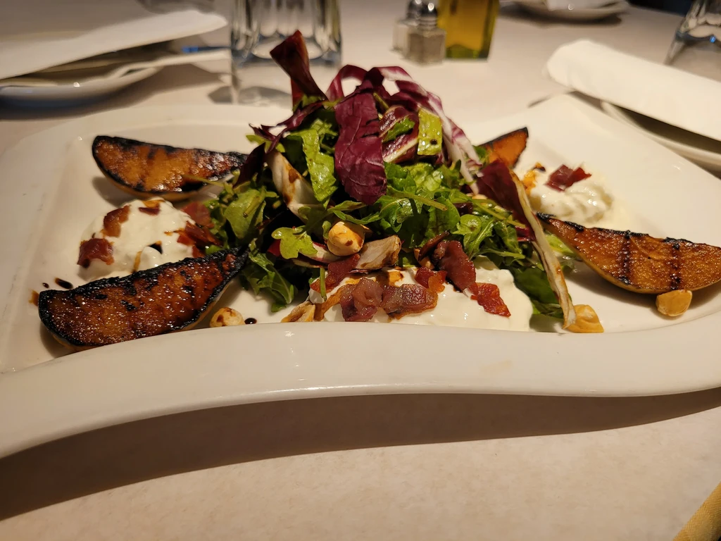 Salad with greens, cheese, pear, bacon, and hazelnuts on a white plate.