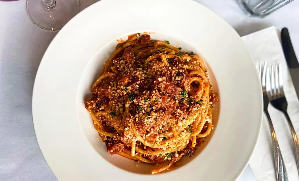 Spaghetti with meat sauce, cheese, and herbs in a white bowl.