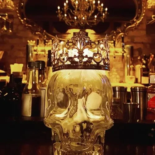 Glass skull-shaped container with gold crown, illuminated on a bar.