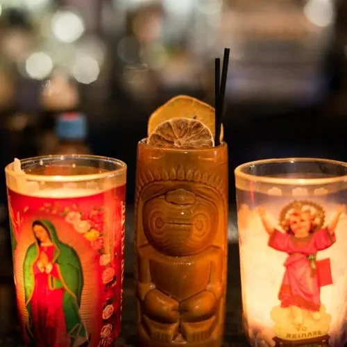 Tiki mug and two religious candles on a bar counter.