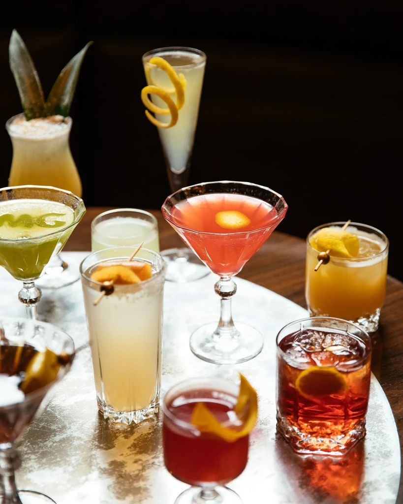 Eight different cocktails, each in a unique glass with a garnish.