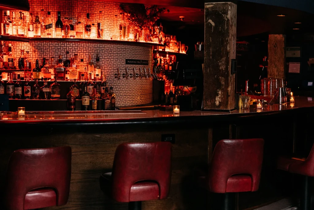 Dimly lit bar with red leather stools and a well-stocked counter.