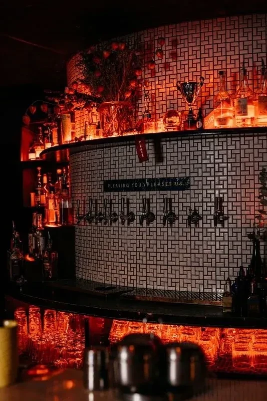Dimly lit bar with a well-stocked counter and reflective surfaces.