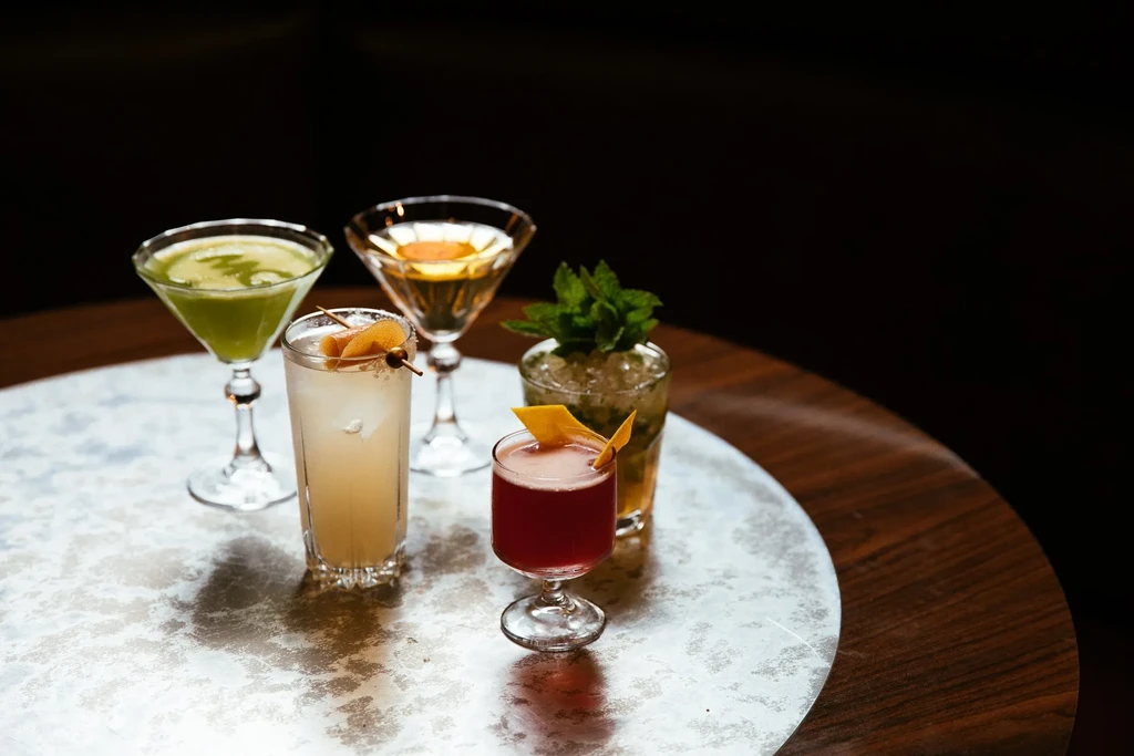 Four cocktails, distinct glasses and garnishes, on a silver tray.