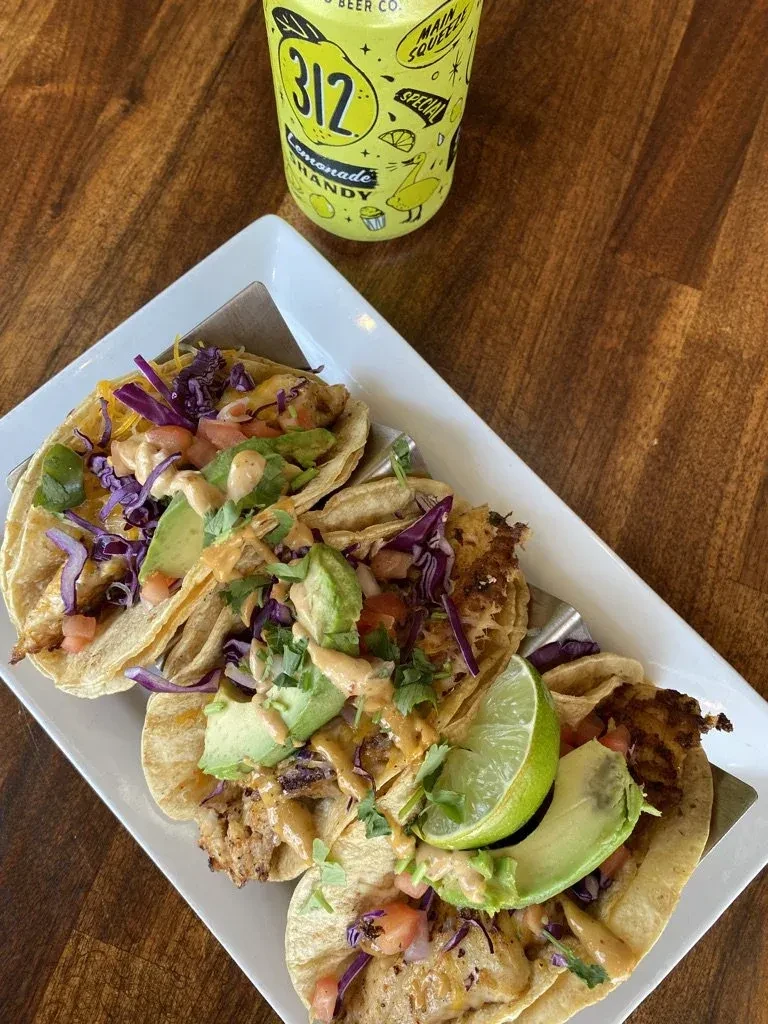 Three tacos with lime and a lemonade on a wooden table.