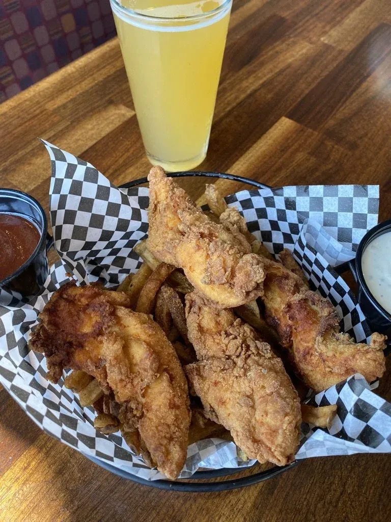 Fried chicken tenders, fries, sauces, and beer on a wooden table.