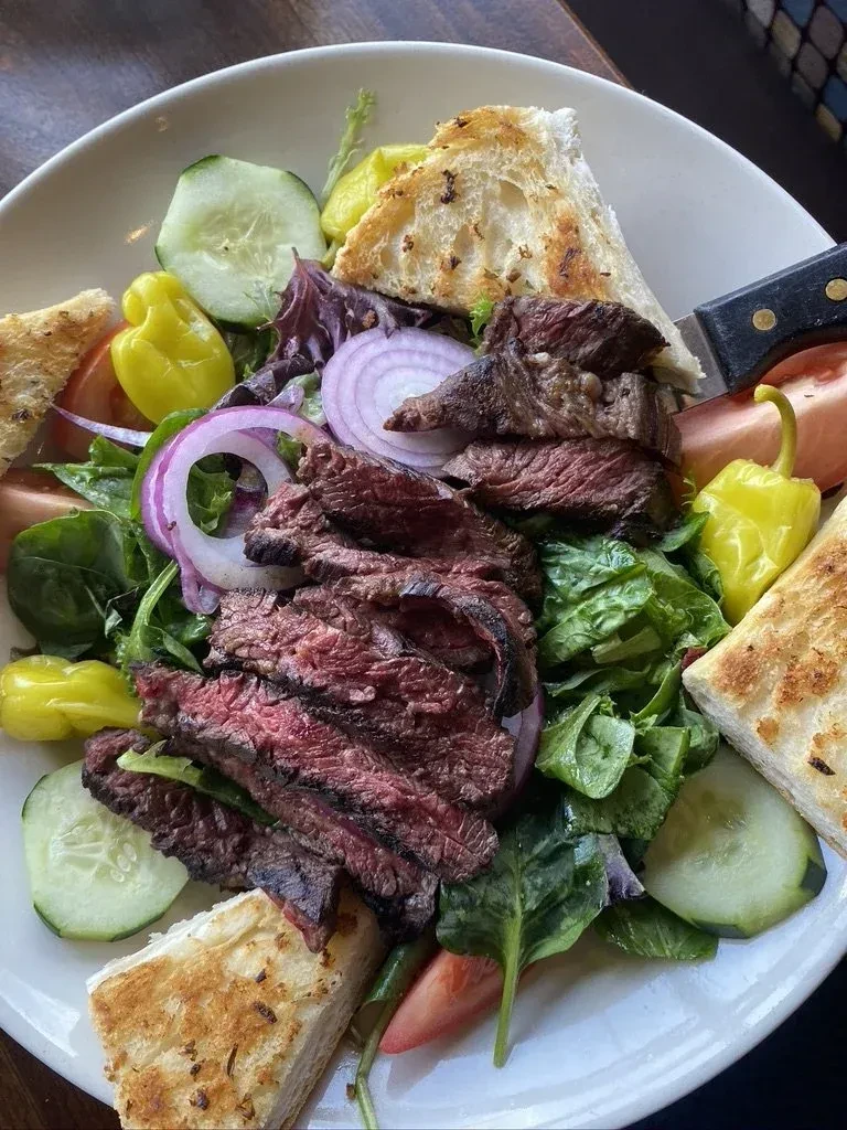 Overhead steak salad with medium-rare steak, mixed greens, vegetables, and croutons.