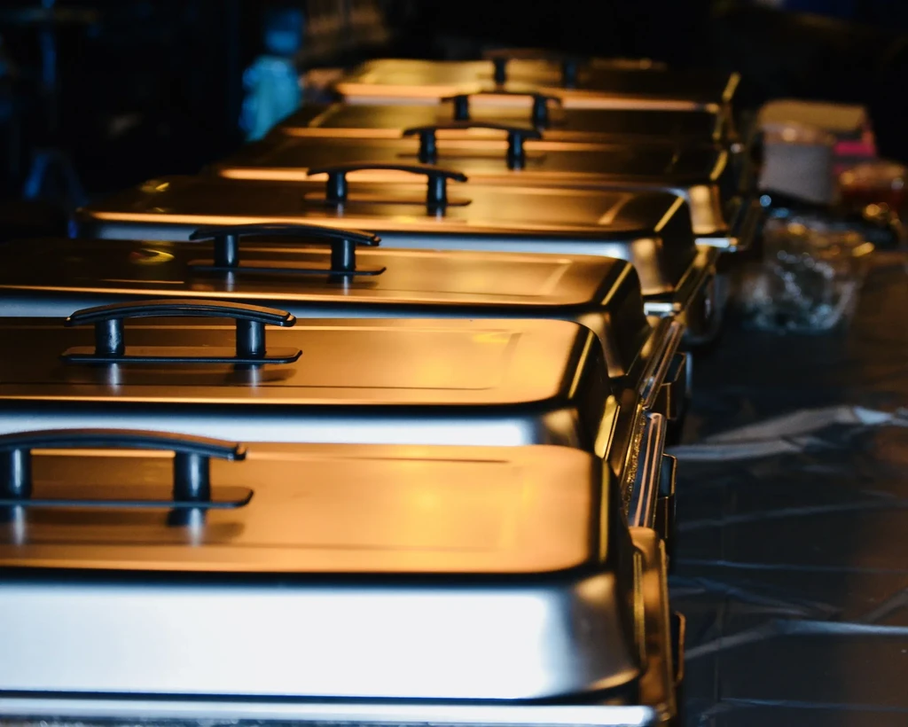 Row of metallic chafing dishes reflecting warm golden light.
