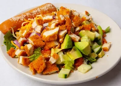 Hearty fried chicken salad with avocado, cheese, and a breadstick.