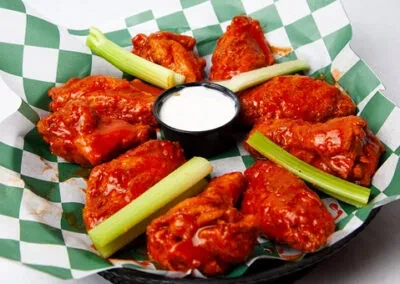 Close-up of buffalo wings with celery and creamy dipping sauce.