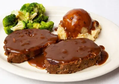 Meatloaf, mashed potatoes, and broccoli with brown gravy on a plate.
