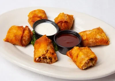 Golden-brown fried rolls, two sauces, and lettuce on a white plate.