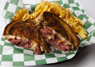 Deli sandwich with corned beef, cheese, sauerkraut, fries, and pickle.